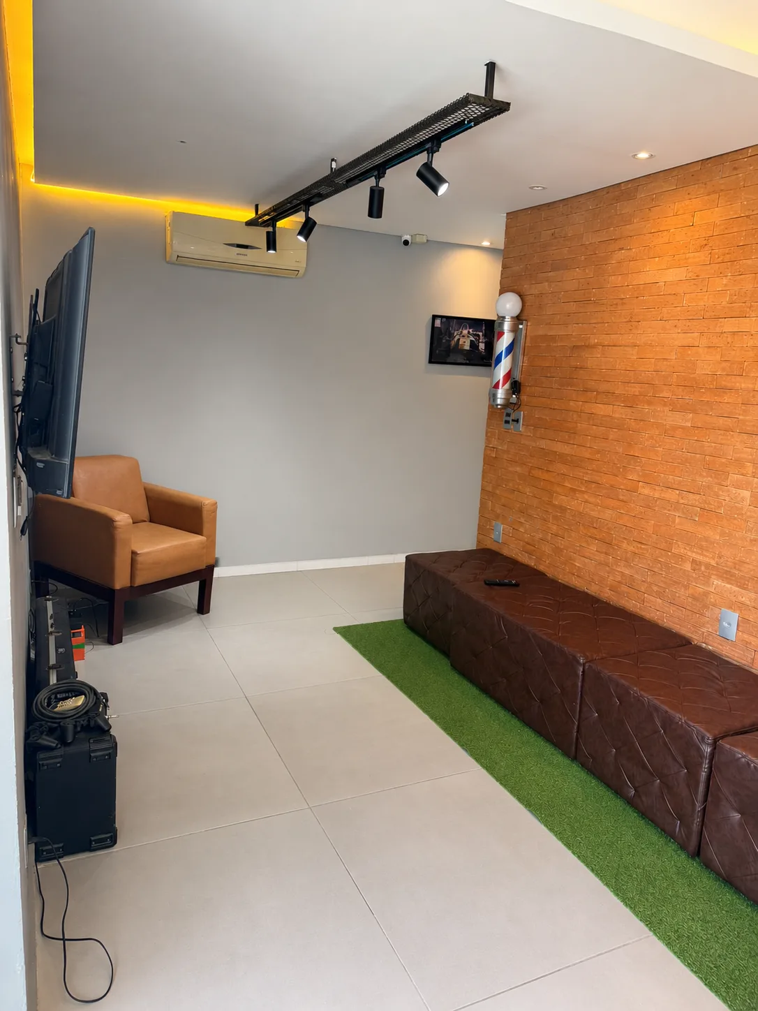Lounge de espera da barbearia Mutari com parede de tijolinho e barber pole